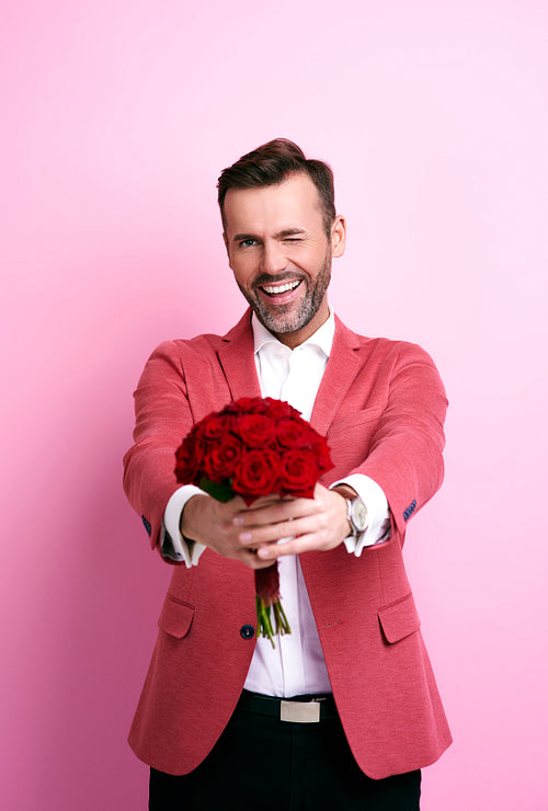 Smiling man winking and giving bunch of roses