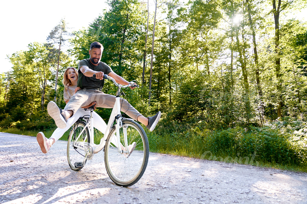 Exuberant couple sharing a bicycle in nature