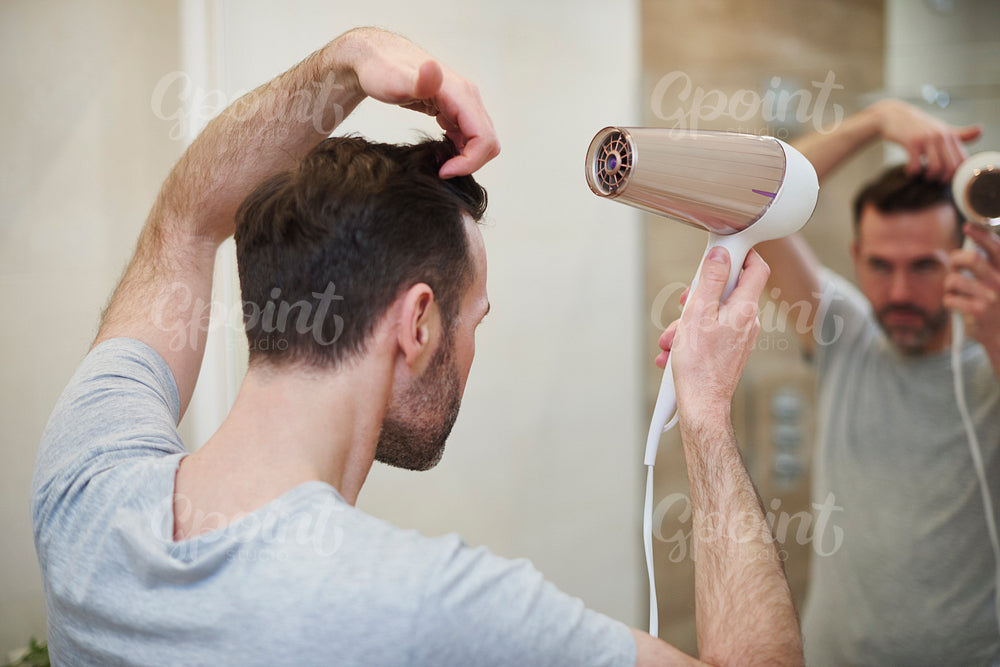 Rear view of man drying his hair in bathroom