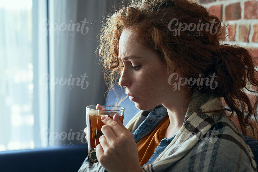 Caucasian red head woman cold and drinking hot tea in the living room