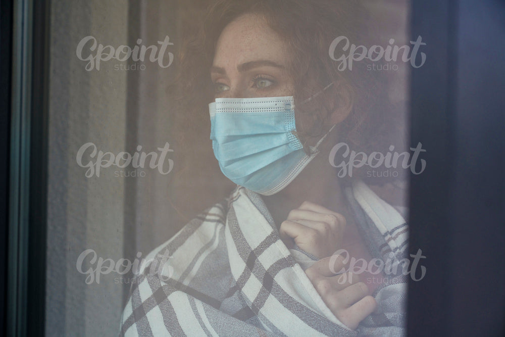 Caucasian red head woman with protective mask standing indoors next to the window