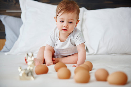 Interested baby girl having fun with eggs