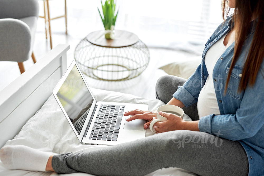 Pregnant woman using laptop while sitting on bed
