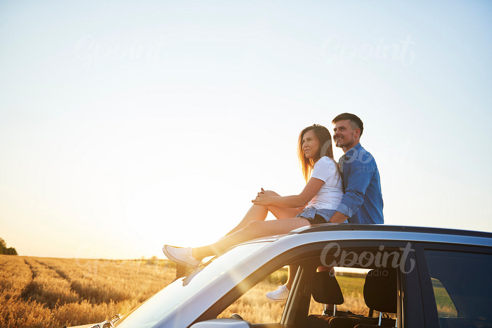 Young couple sitting on car and looking straight ahead.