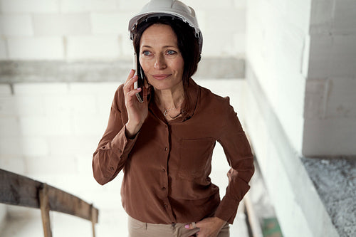 Female mature caucasian engineer moving on the stairs on construction site and talking one mobile phone
