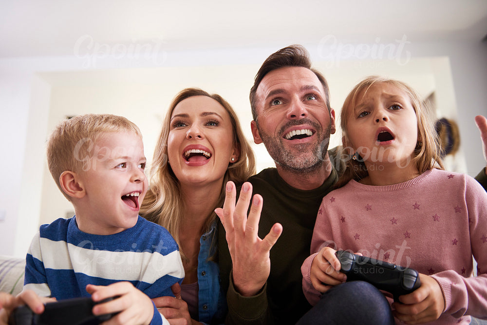 Emotional parents and children playing video game at home