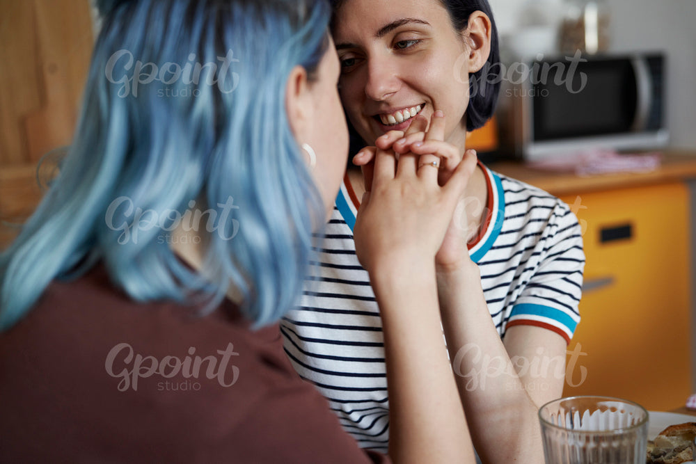 Happy lesbian couple holding hands and sitting in the kitchen