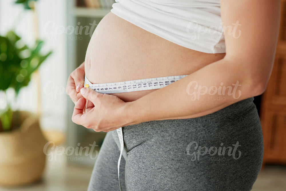 Pregnant woman using tape measure to control the abdomen