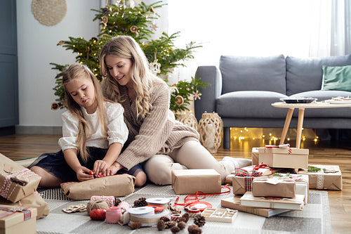 Wide shot of caucasian girl and mother wrapping Christmas gifts