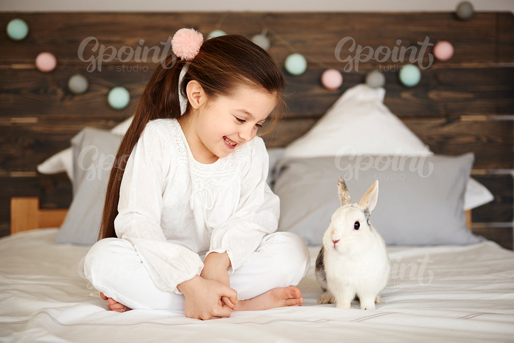 Girl and rabbit sitting on bed