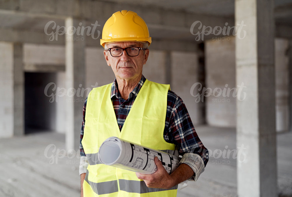 Portrait of caucasian senior engineer holding plans and standing on construction site
