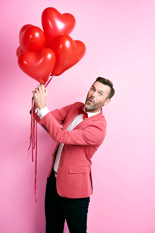 Surprised man holding heart shape balloons