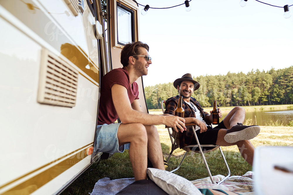 Two young male friends spending time on the camper side and drinking beer 
