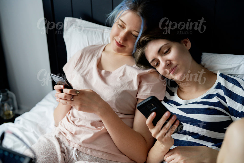 Romantic lesbian couple lying in bed with mobile phones
