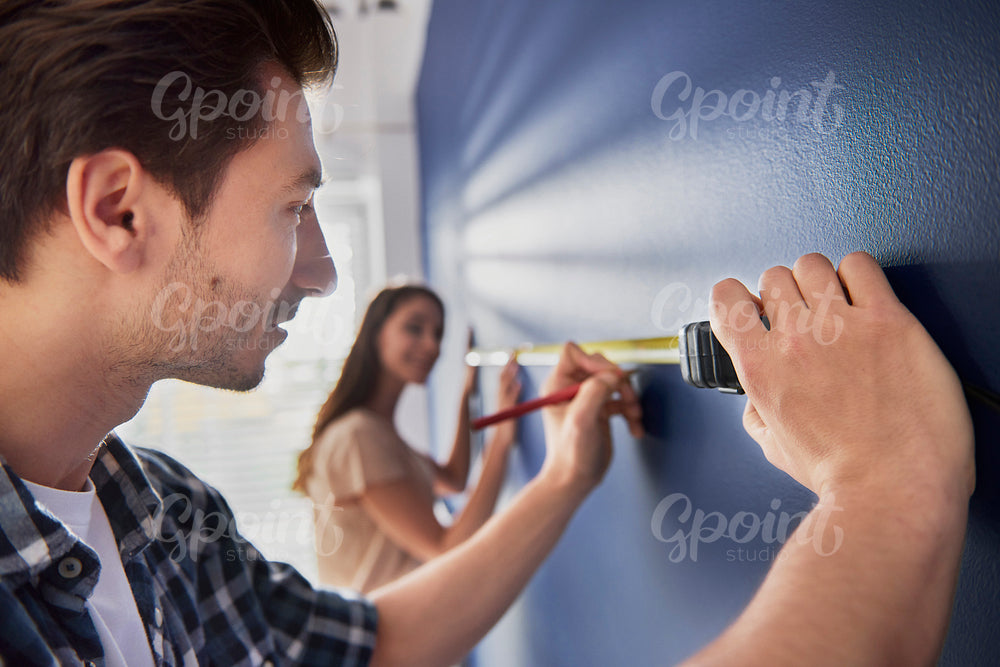 Couple taking measures on wall with tape measure