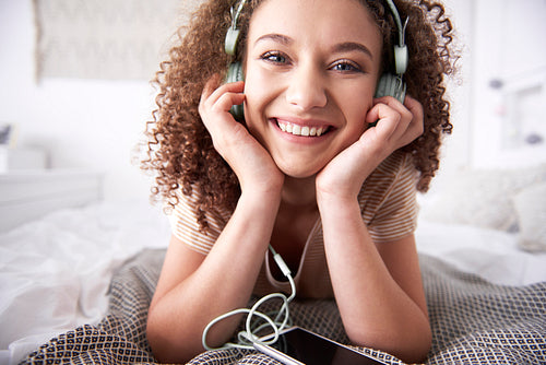 Portrait of smiling teenage girl listening to music in bedroom