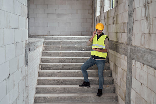 Caucasian engineer standing on stairs and browsing digital tablet on construction site