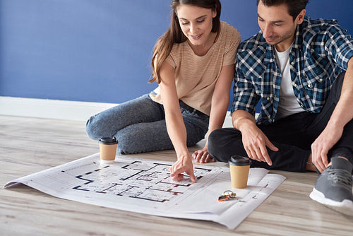 Couple sitting on floor and looking at house blueprint