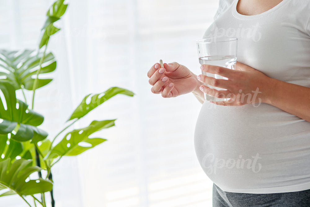 Pregnant woman about to take a pill and drink water