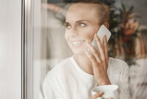 Happy businesswoman looking through window and talking by mobie phone