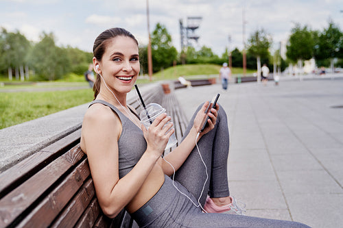 Portrait of smiling athletic woman sitting outdoors with isotonic drink