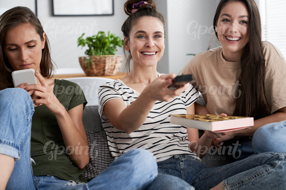 Three friends watching TV with a box of chocolates