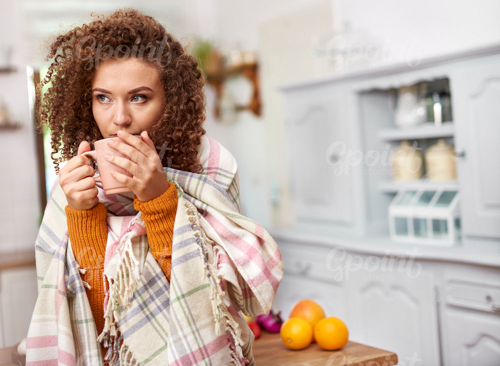 Young woman wrapped in blanket drinking hot tea