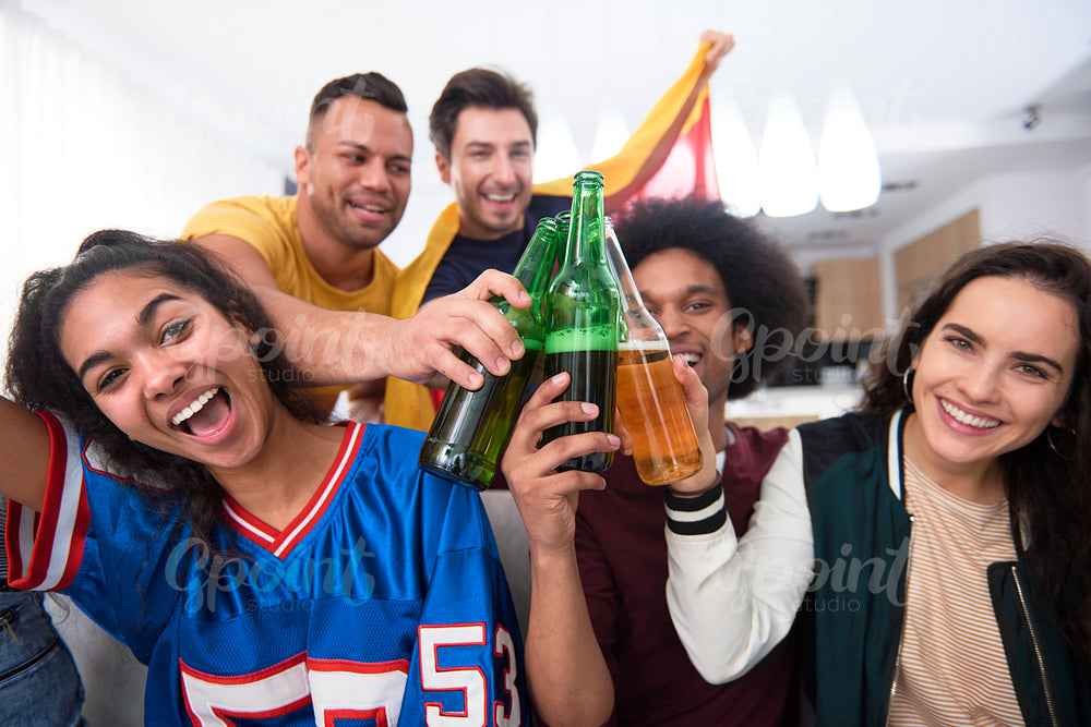 Group of smiling friends toasting with beer bottle at home