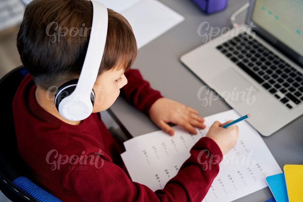 Top view of boy doing homework while e-learning