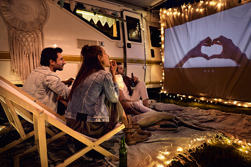 Group of young cheerful people watching a movie on camping site