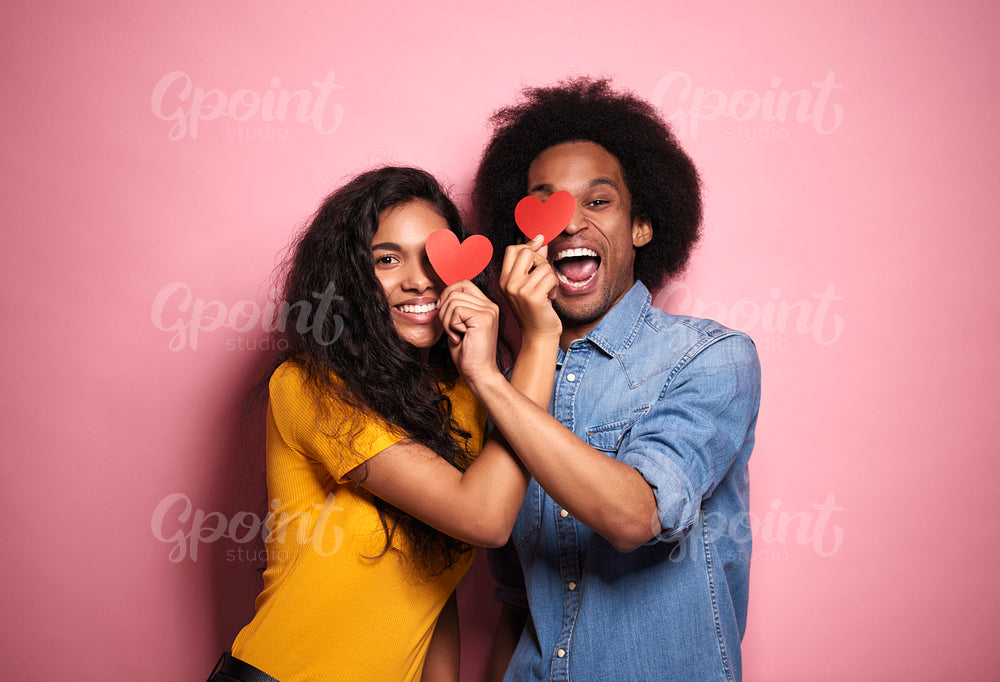 African couple covering eyes by hearts in studio shot.