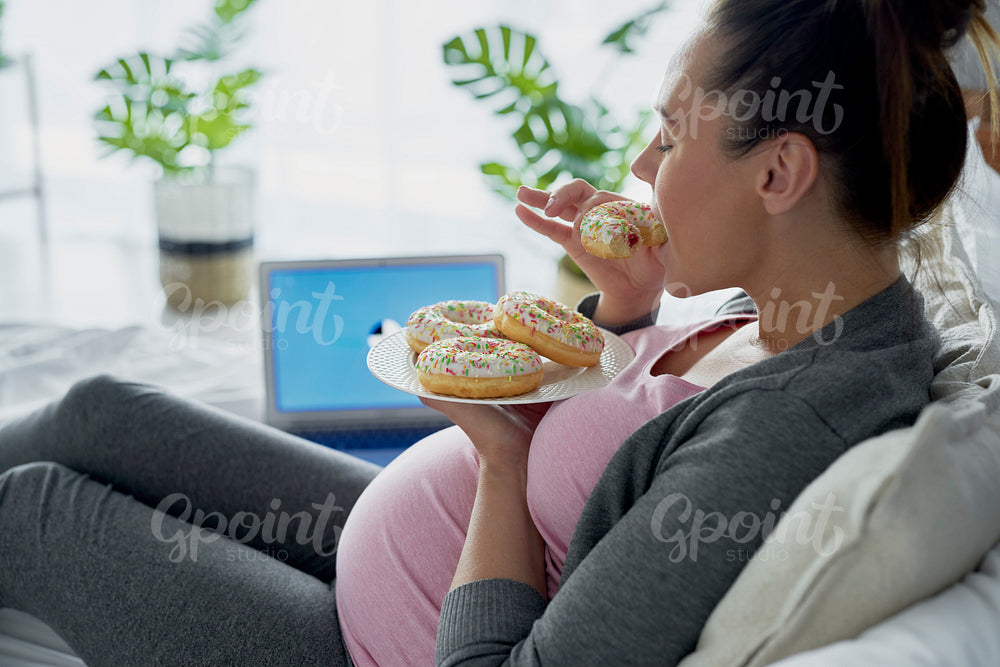 Pregnant woman eating donuts in front of computer