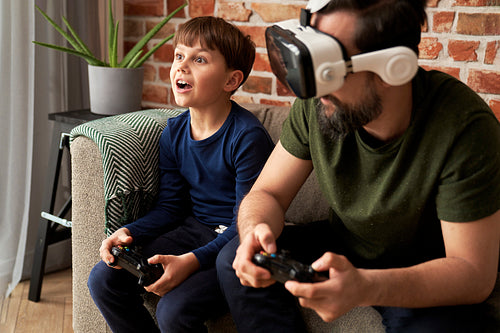 Father wearing VR glasses playing with son at home