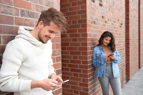 Smiling man using smart phone and woman in the background