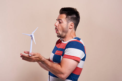 Portrait of man blowing model of wind turbine