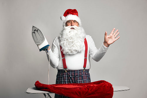 Shocked caucasian Santa Claus ironing trousers for Christmas