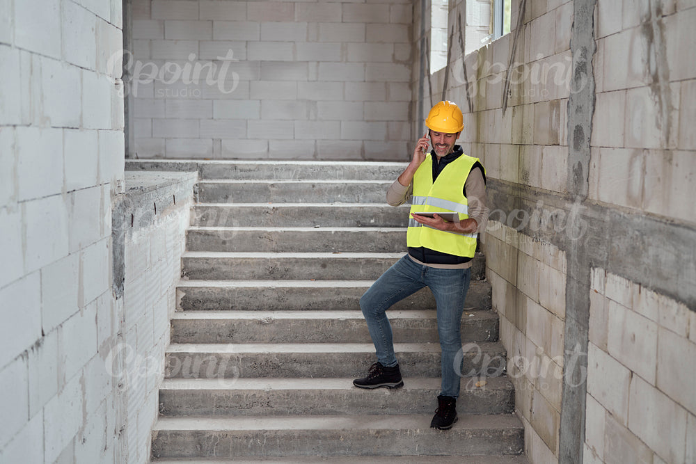 Caucasian engineer standing on stairs and browsing digital tablet on construction site