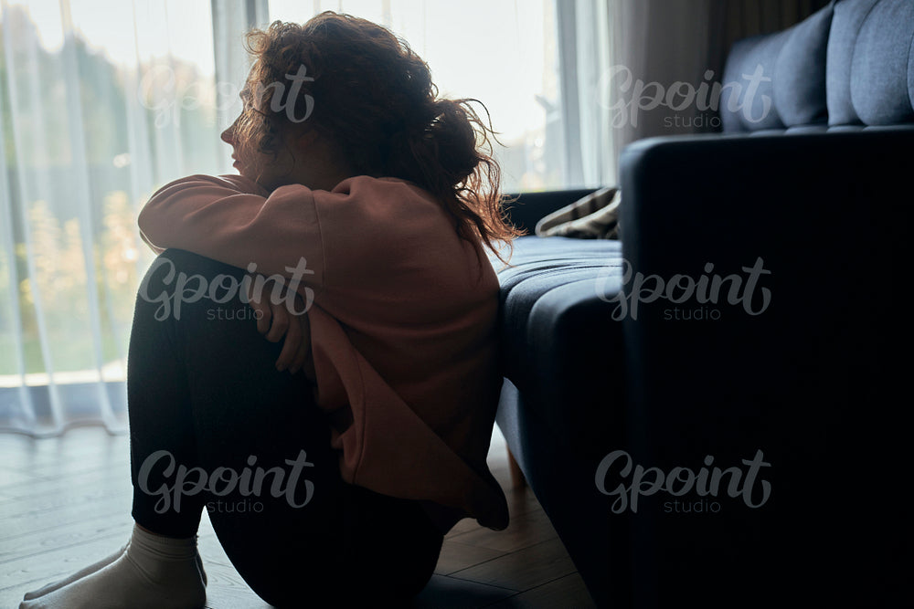 Depressed young caucasian woman flooring in silence  next to sofa