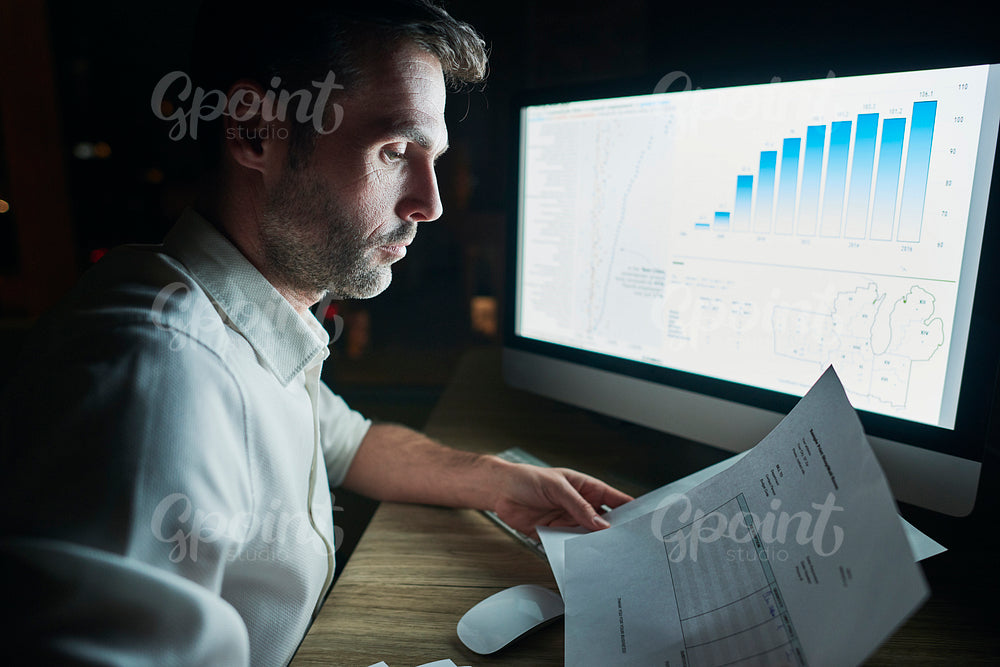 Side view of mature man analyzing documents at night