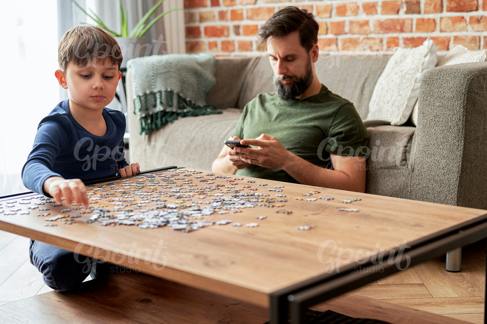 Boy solving jigsaw puzzle during father using