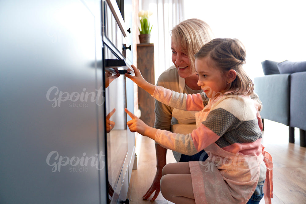 Side view of girl and grandma watching biscuits in kitchen oven