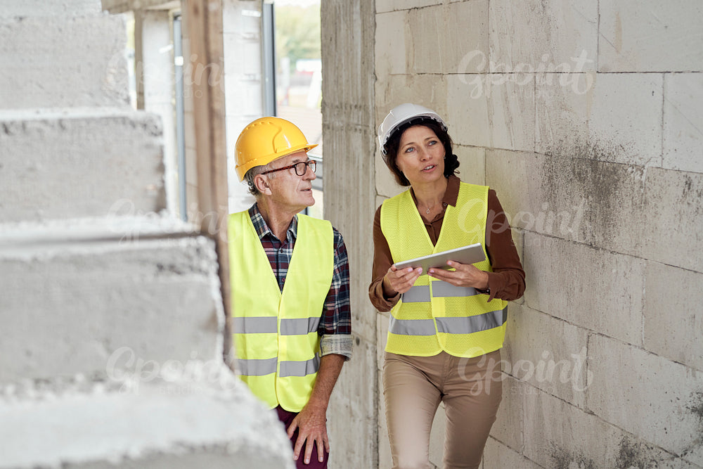 Two caucasian engineers standing on stairs, looking up and discussing over digital tablet on the construction site