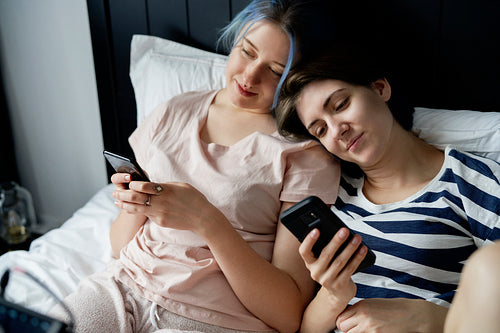 Romantic lesbian couple lying in bed with mobile phones