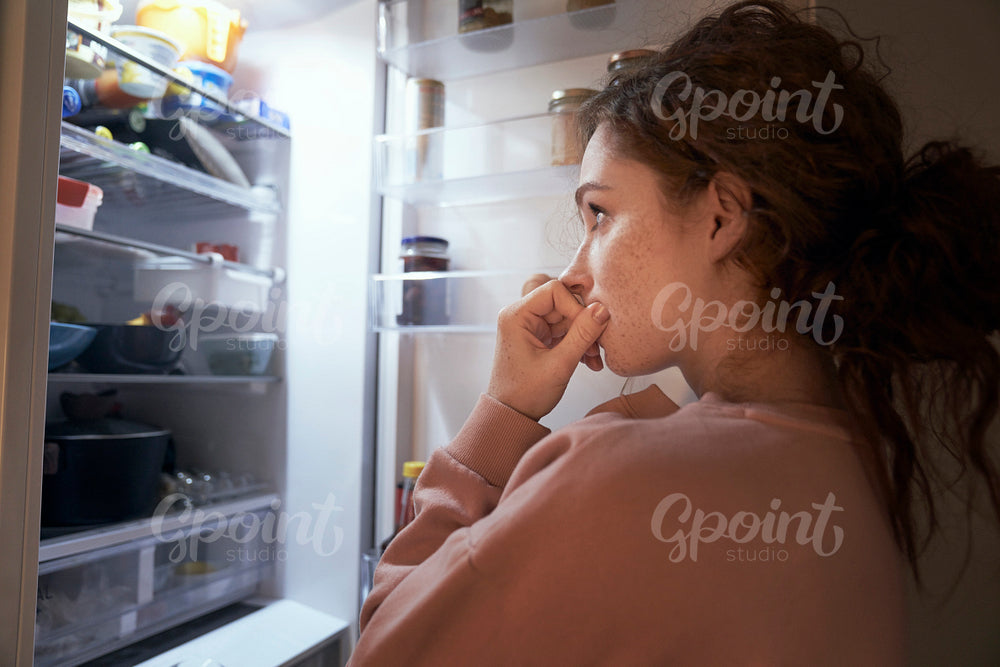 Undecided young caucasian woman checking fridge for some food at night