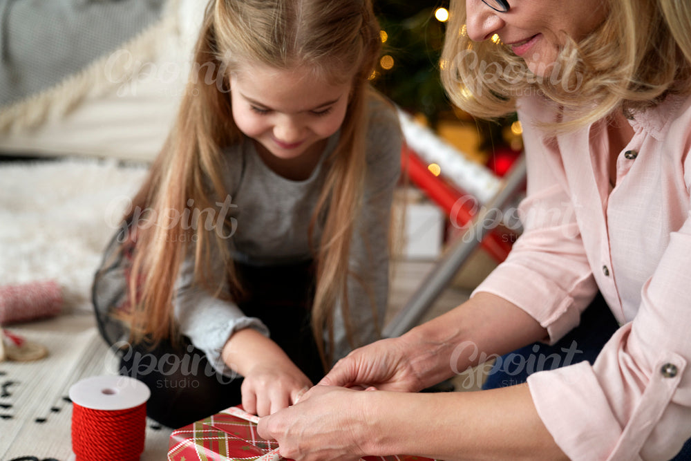 Happy grandmother and girl packing a gift for Christmas