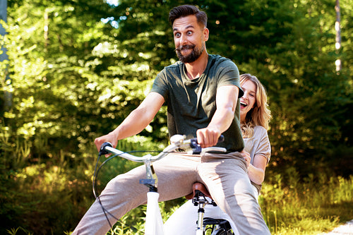 Happy couple having fun on a bike in the woods