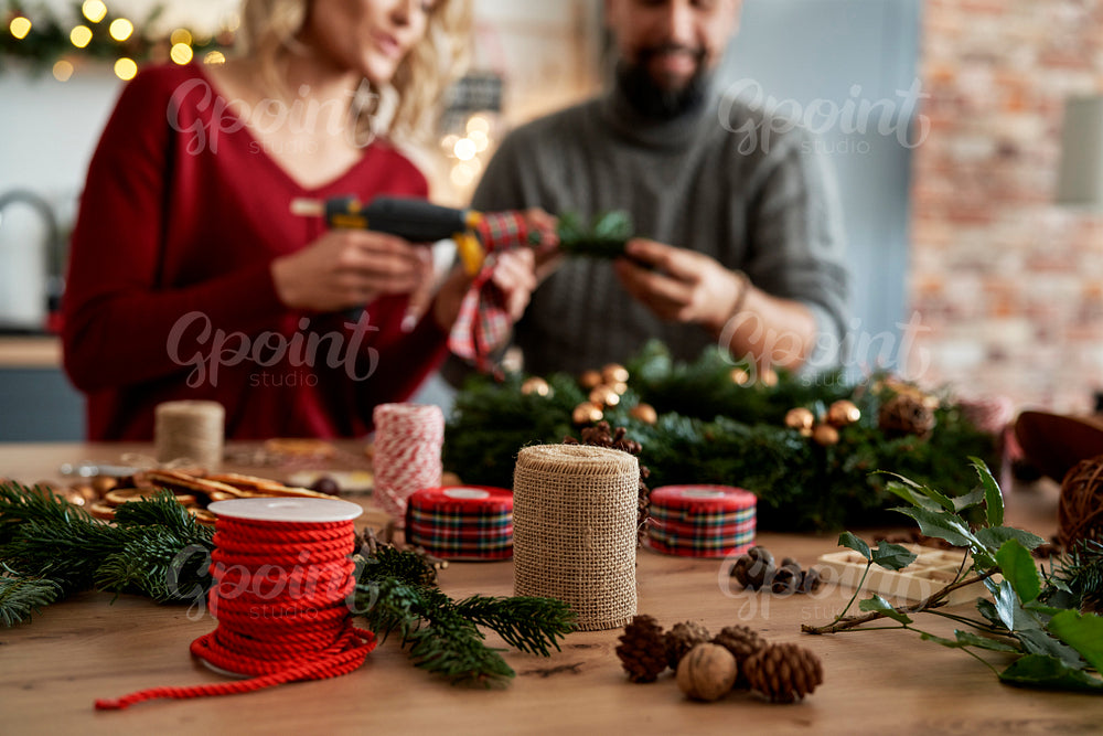 Table full of Christmas decorations and couple making Christmas wreath