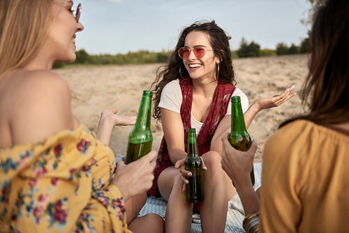 Three woman sitting on the beach and drinking beer