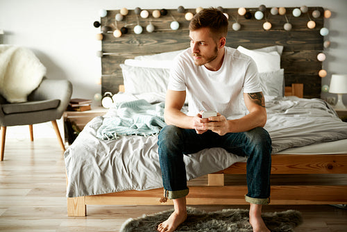 Man with mobile phone sitting on bed