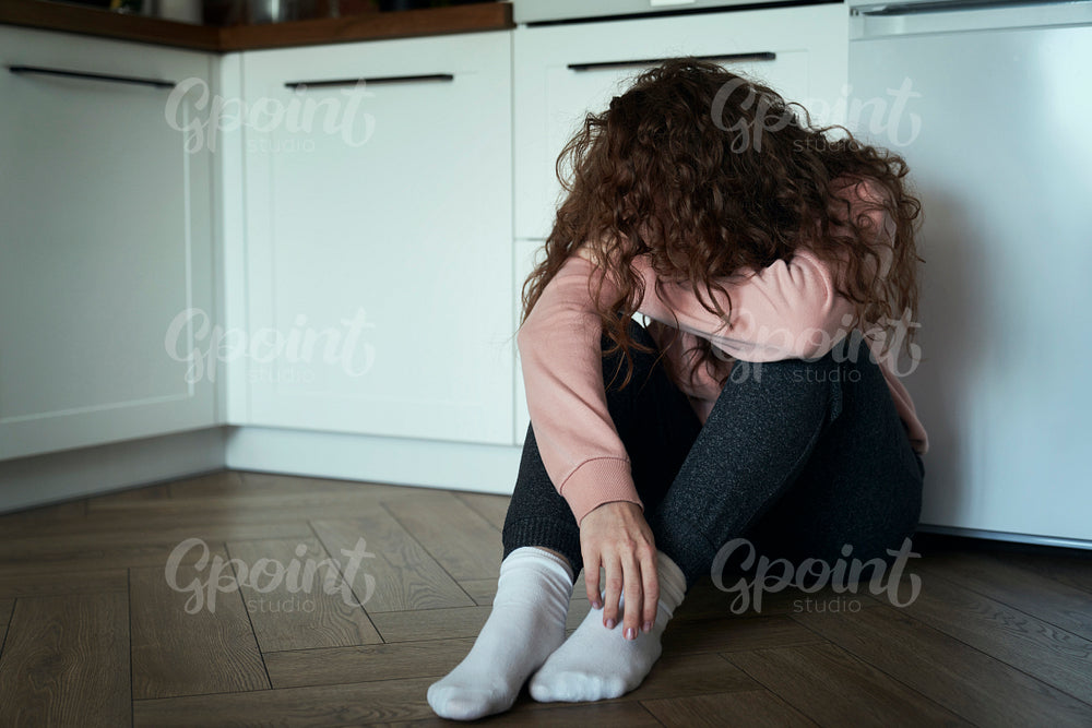 Broken young caucasian woman  with hidden face sitting on floor in the kitchen